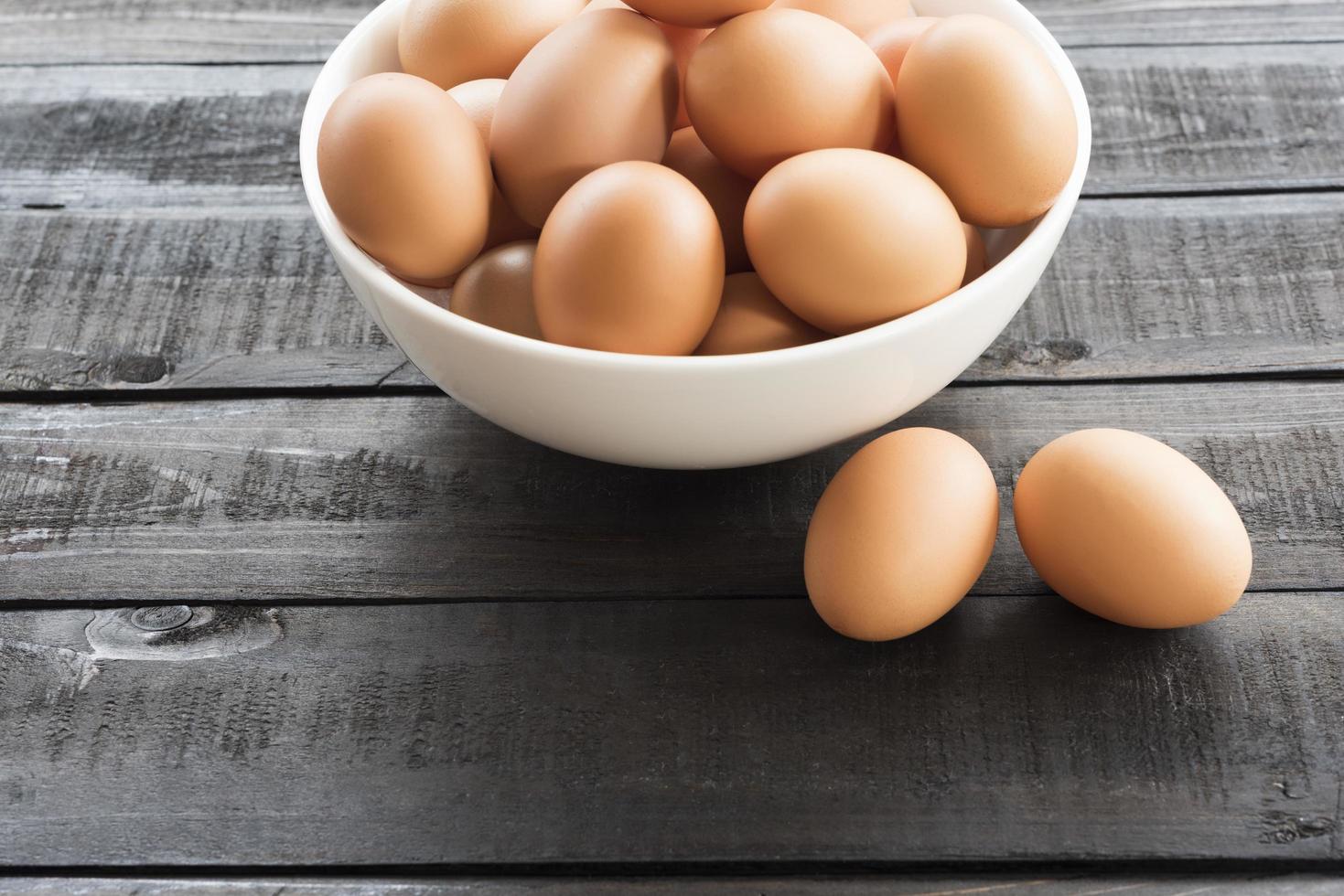 Chicken eggs in a white bowl and chicken eggs outside on a black wooden table photo