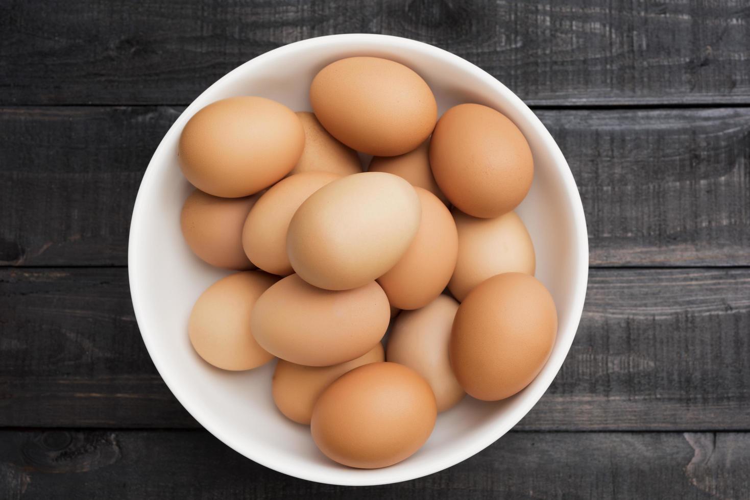 Huevos de gallina frescos en un recipiente blanco sobre una mesa de madera negra foto