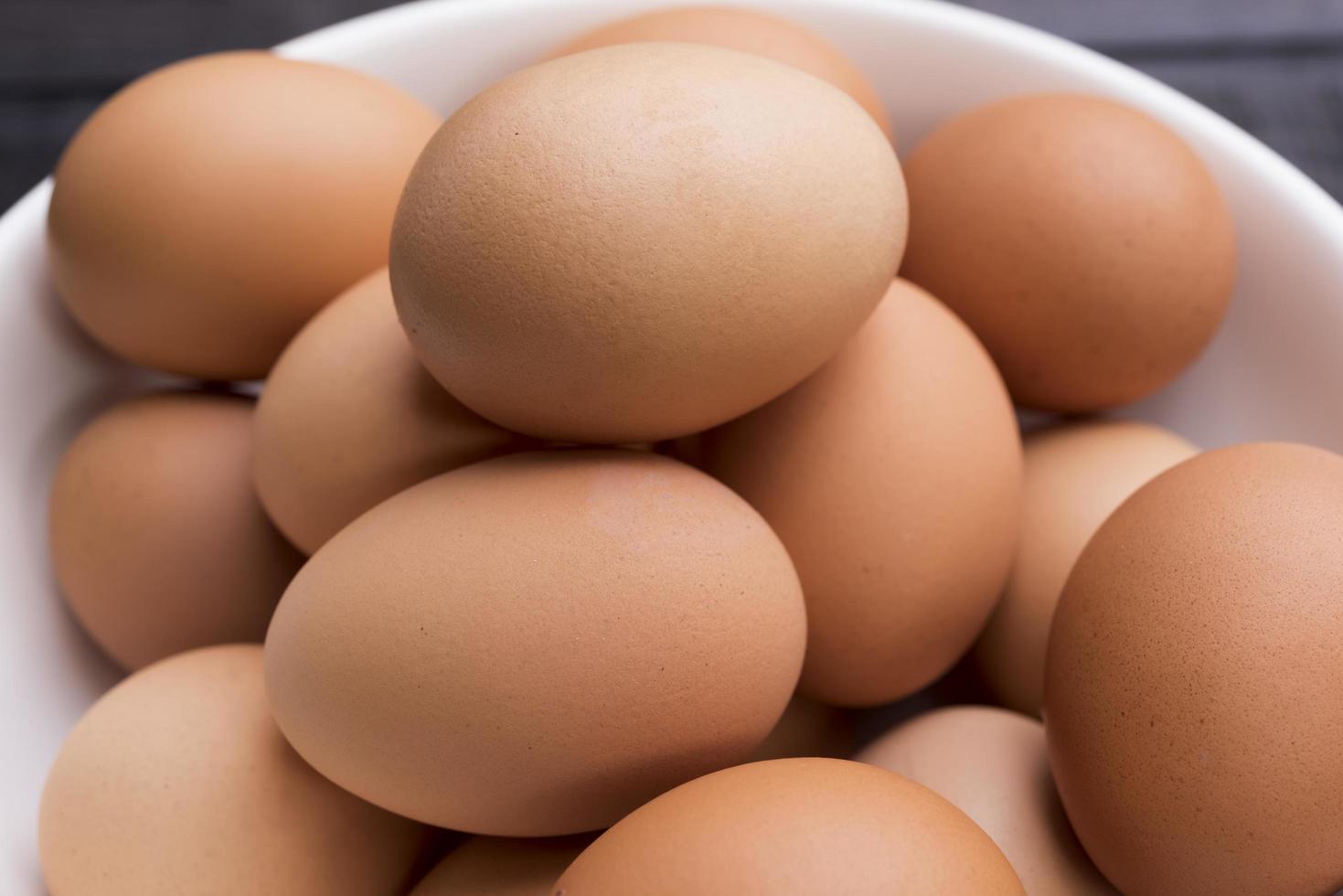 Cerca de huevos de gallina frescos en un recipiente blanco sobre una mesa de madera negra foto