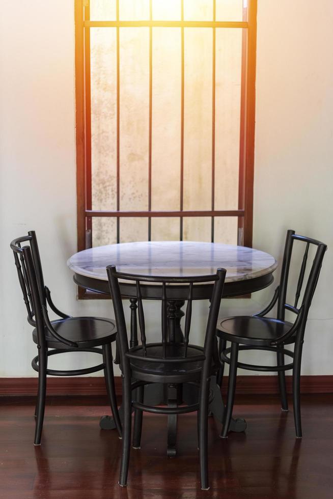 Wooden round table and chairs near a window with rays of sunlight on a wooden floor and white wall photo
