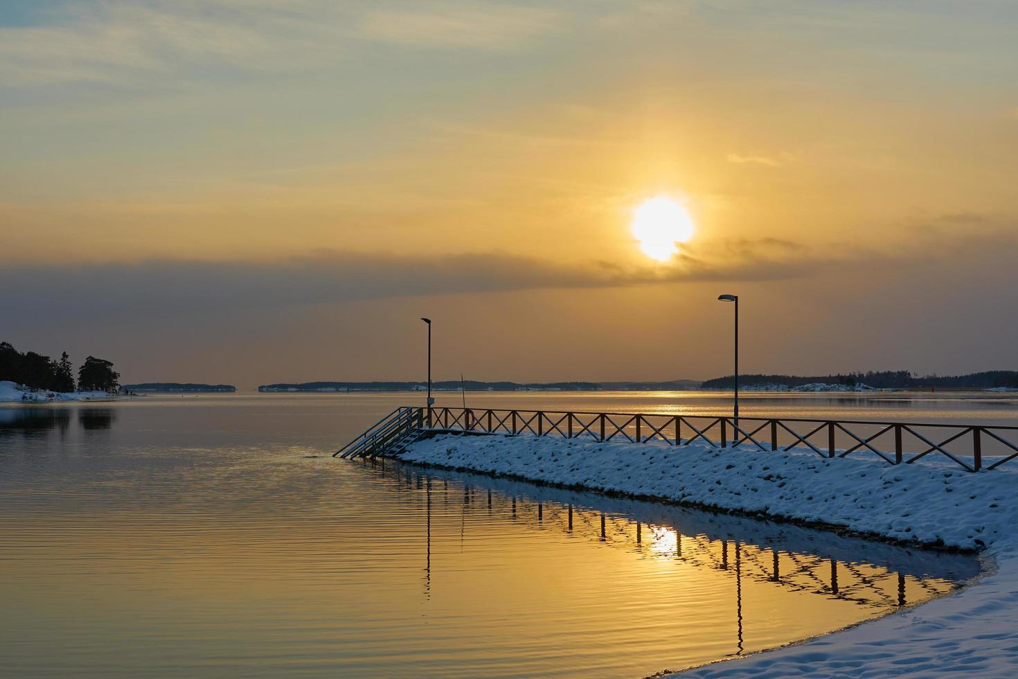 Snow-covered pier at sunset by the sea photo