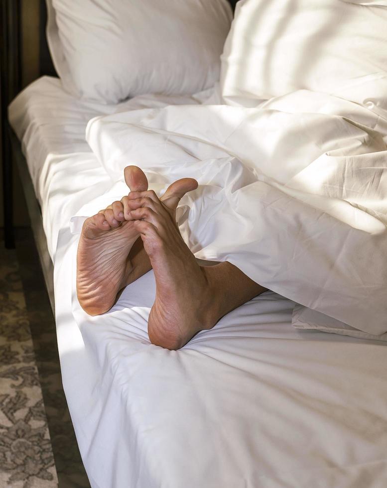 Feet of a sleeping person sticking out from under a warm and comfortable blanket on the bed, bare heels photo