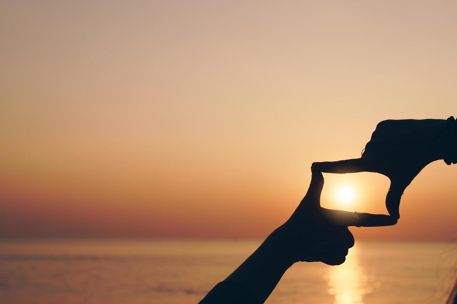 Selective focus of woman's hands making a frame with a finger gesture with sunset or sunrise, female capture sunrise or sunlight outdoors, future planning concept. photo