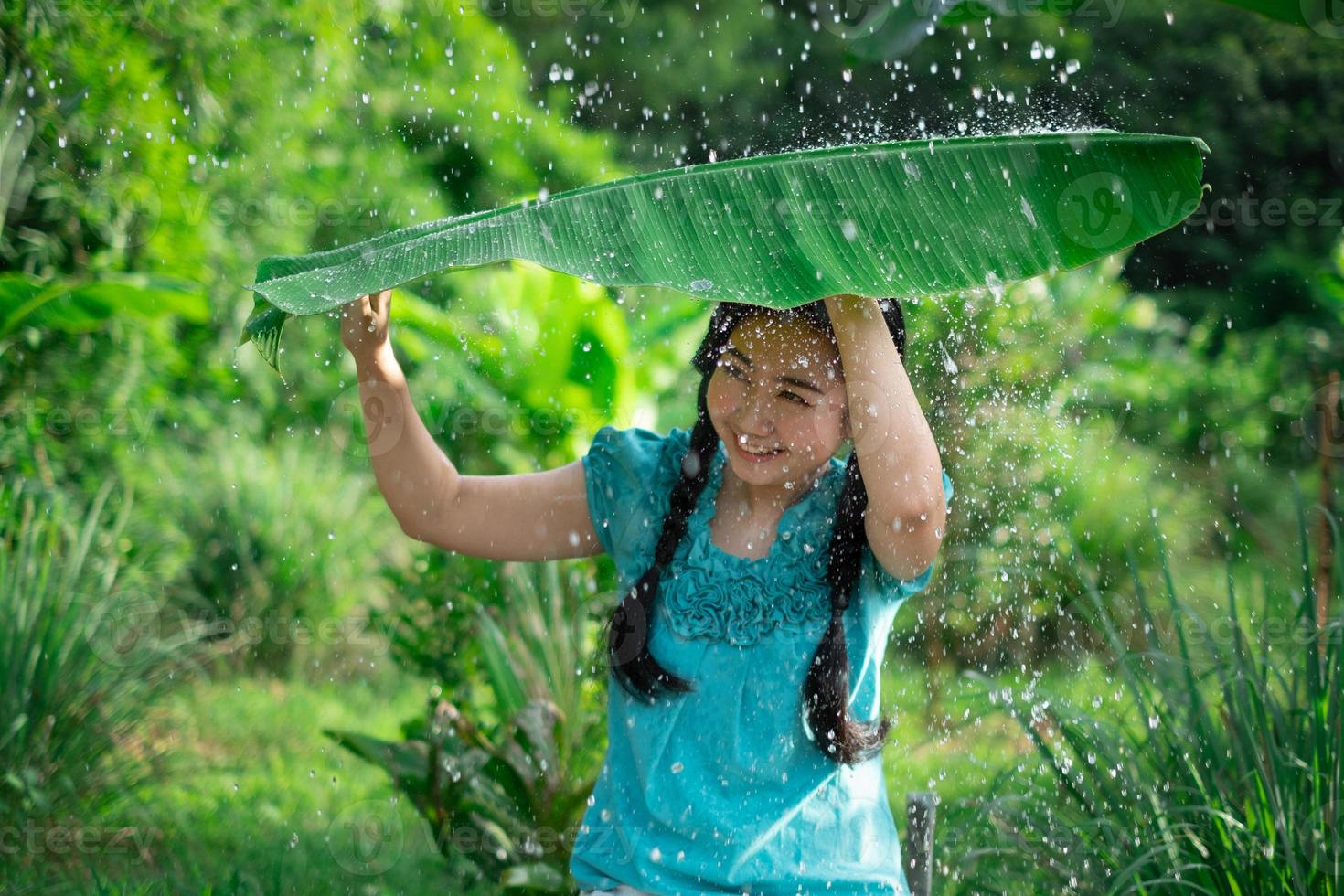 Mujer asiática sosteniendo una hoja de plátano bajo la lluvia foto