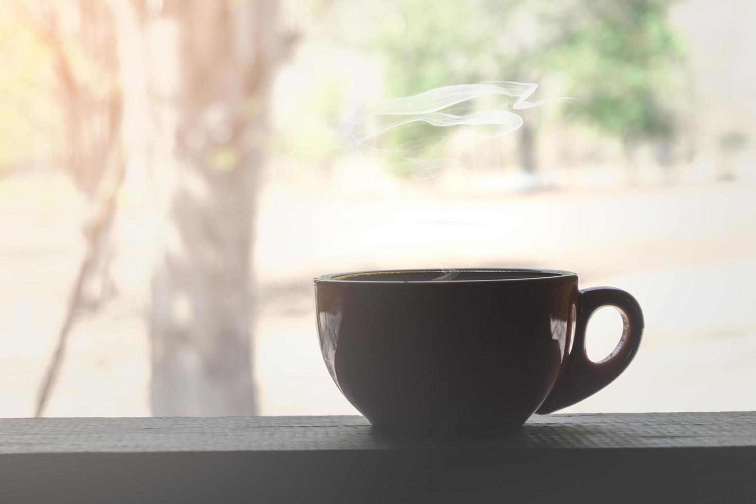 Close up of a brown coffee cup with smoke on a wooden table with a view of trees photo
