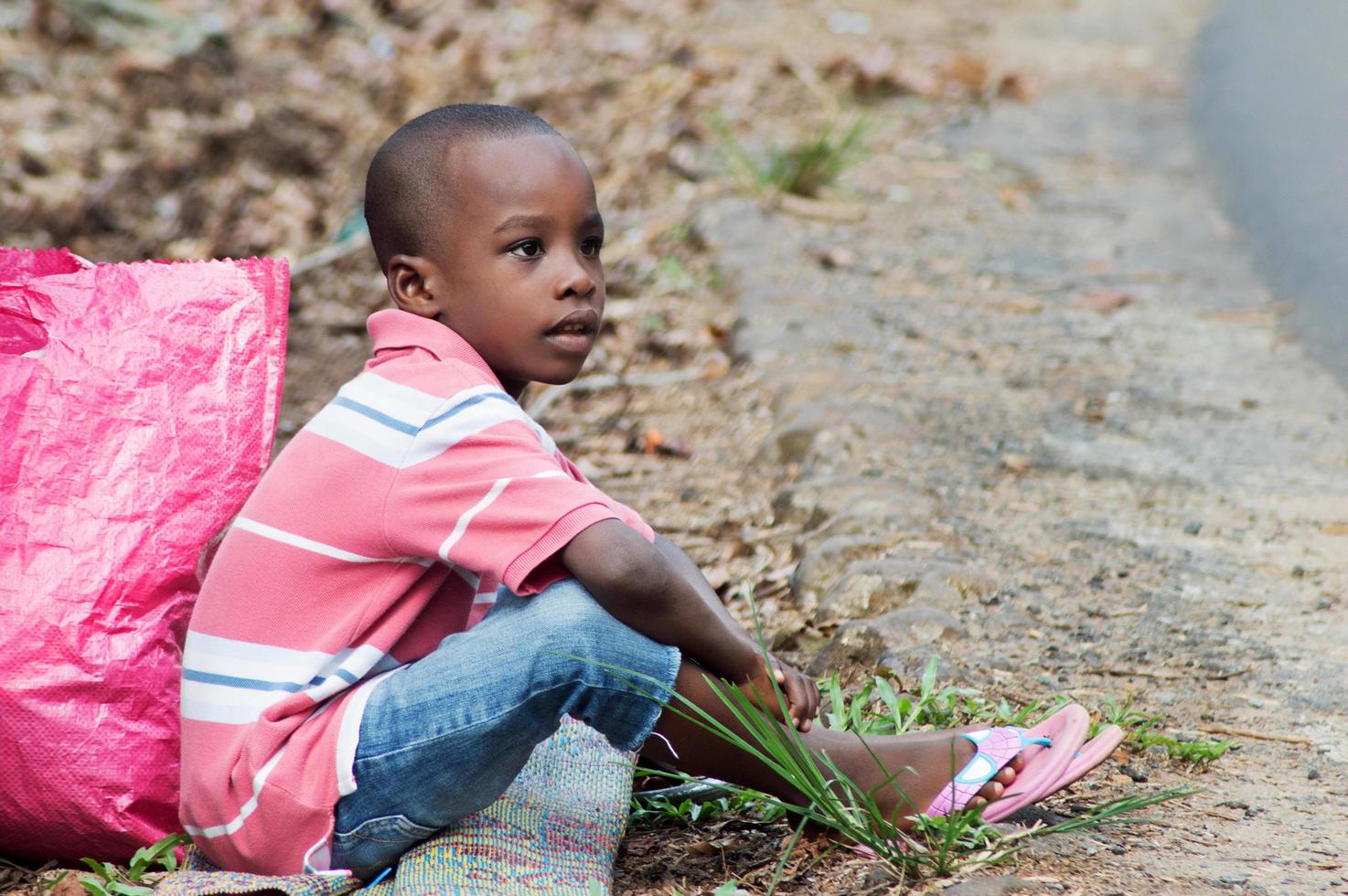 Child sitting on the ground and beside him a bag photo