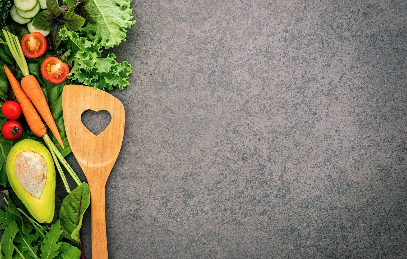 comida sana y concepto de cocina con una espátula de madera y verduras sobre fondo de piedra oscura. foto