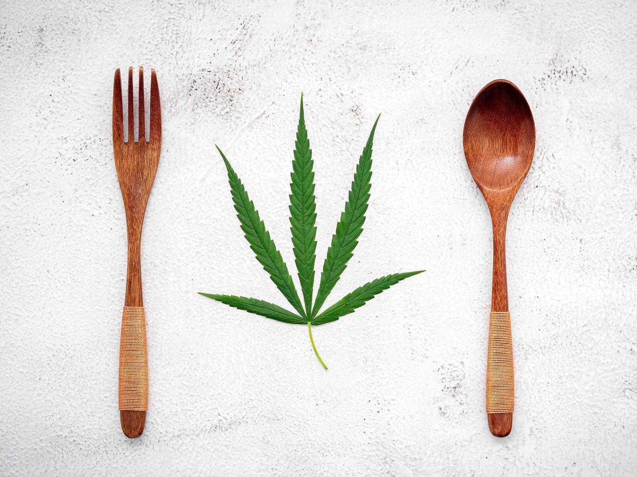 Food conceptual image of a hemp leaf with a spoon and fork on white concrete background photo