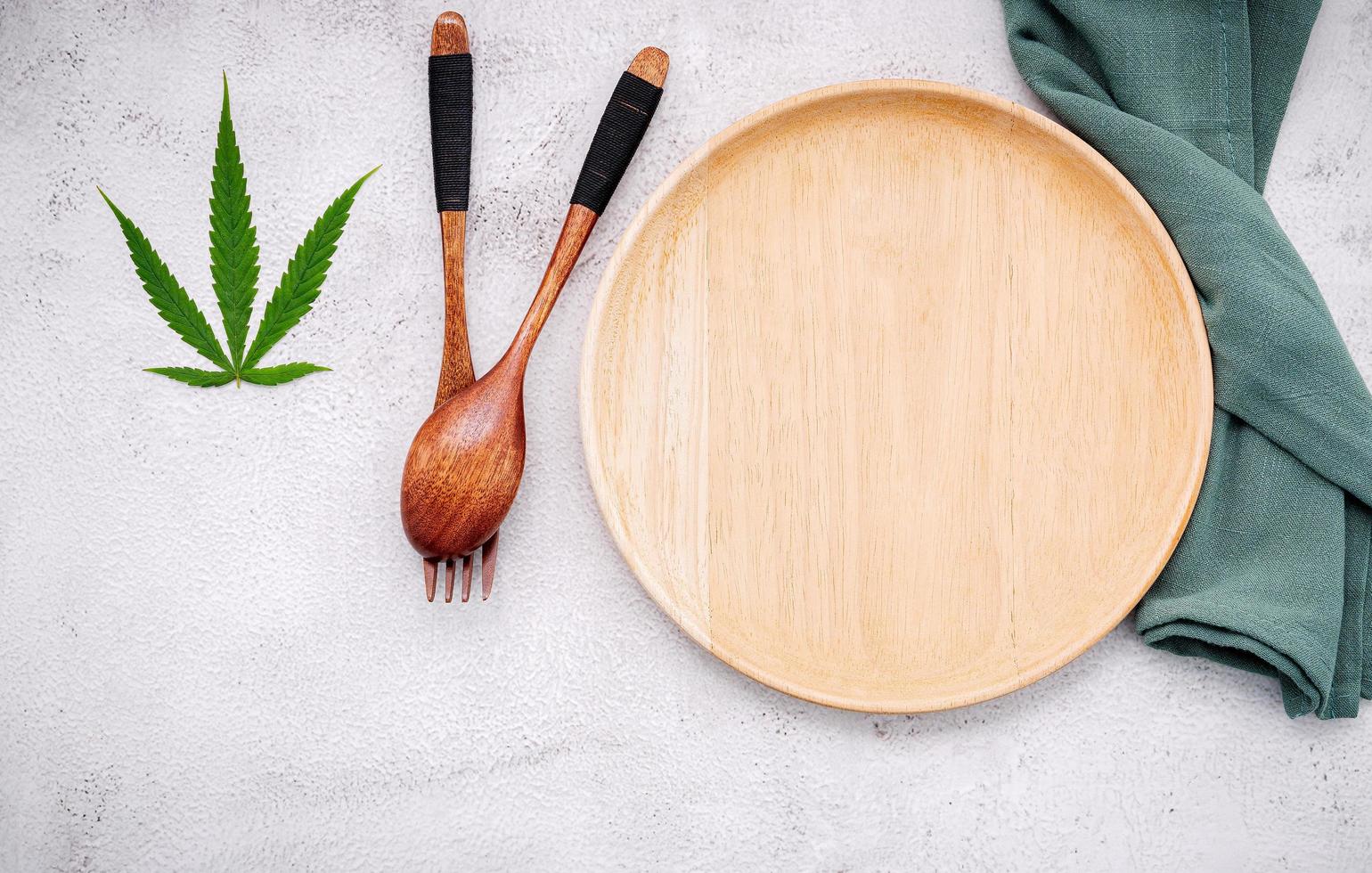 Food conceptual image of a hemp leaf with a spoon and fork on white concrete background photo