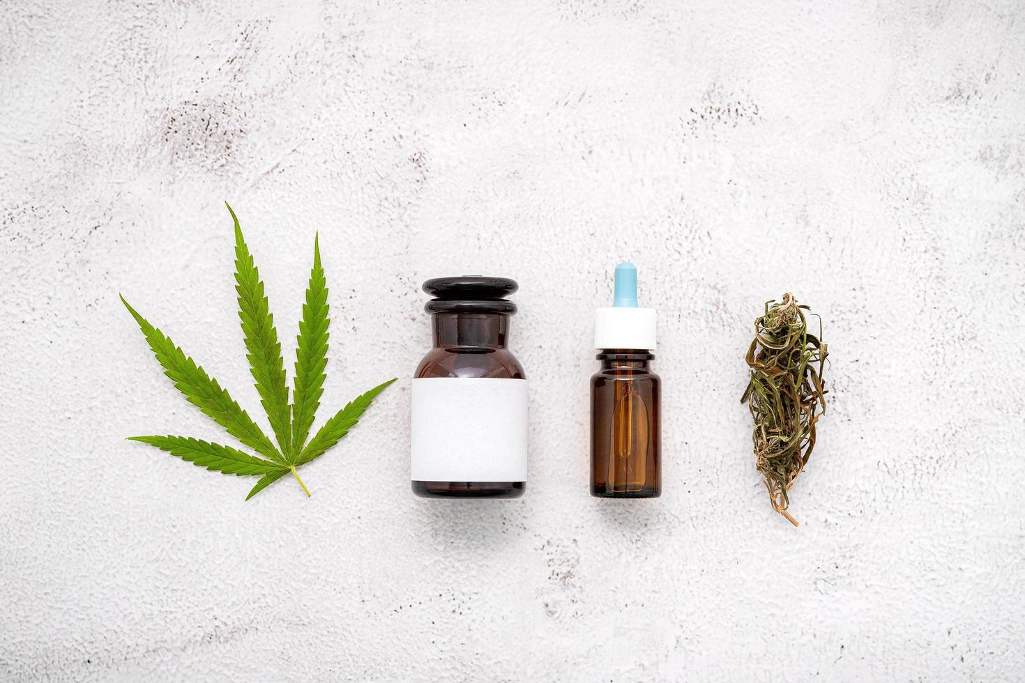 Glass bottle of hemp oil with a white mortar and hemp leaves set up on a concrete background, aromatherapy concept photo