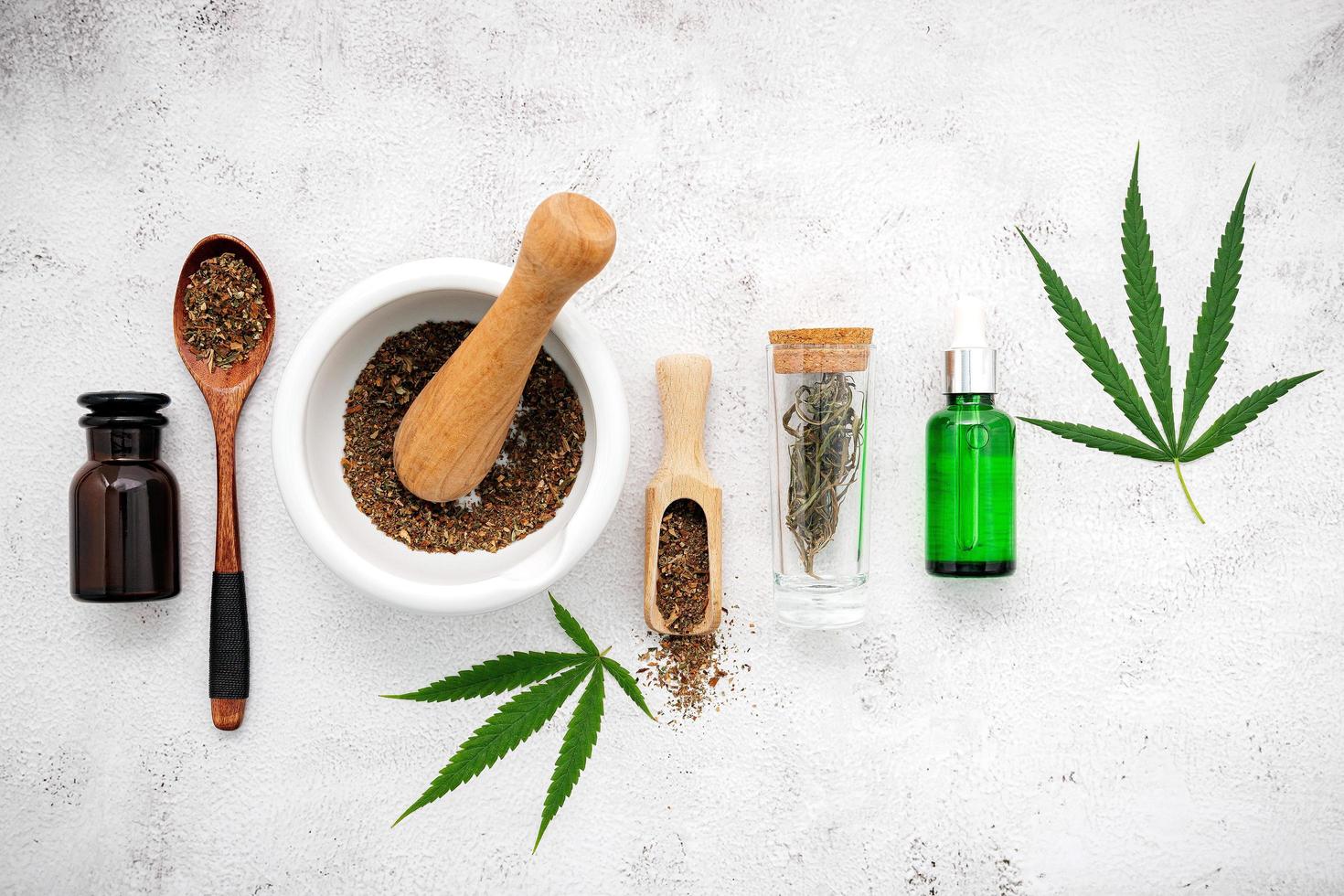 Glass bottle of hemp oil with a white mortar and hemp leaves set up on a concrete background, aromatherapy concept photo