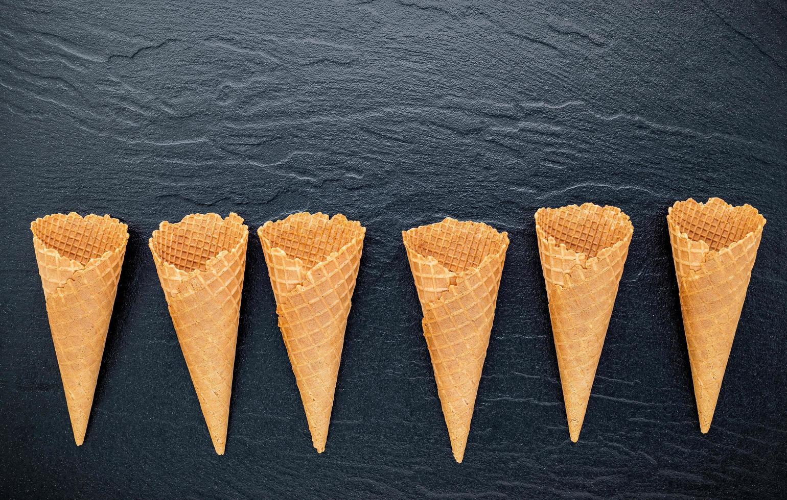Flat lay of ice cream cones on a dark stone background, crispy ice cream cone with copy space for sweets menu design photo