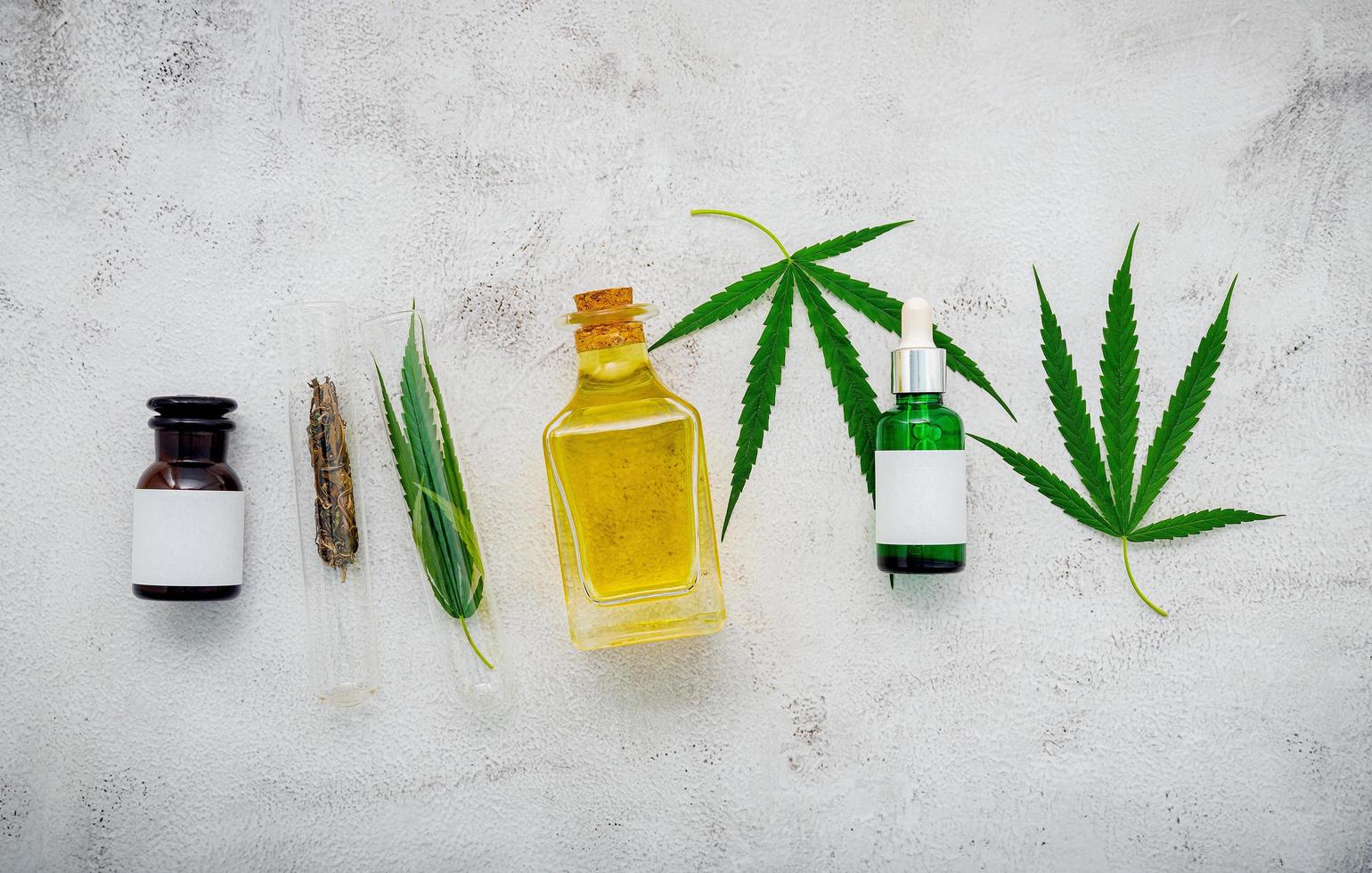 Glass bottles of hemp oil and hemp leaves set up on a concrete background photo