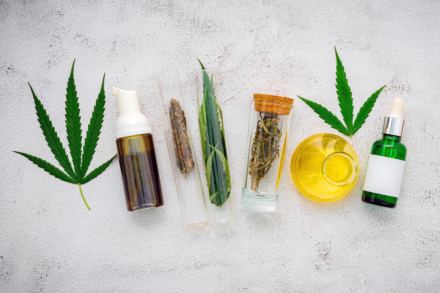 Glass bottles of hemp oil and hemp leaves set up on a concrete background photo