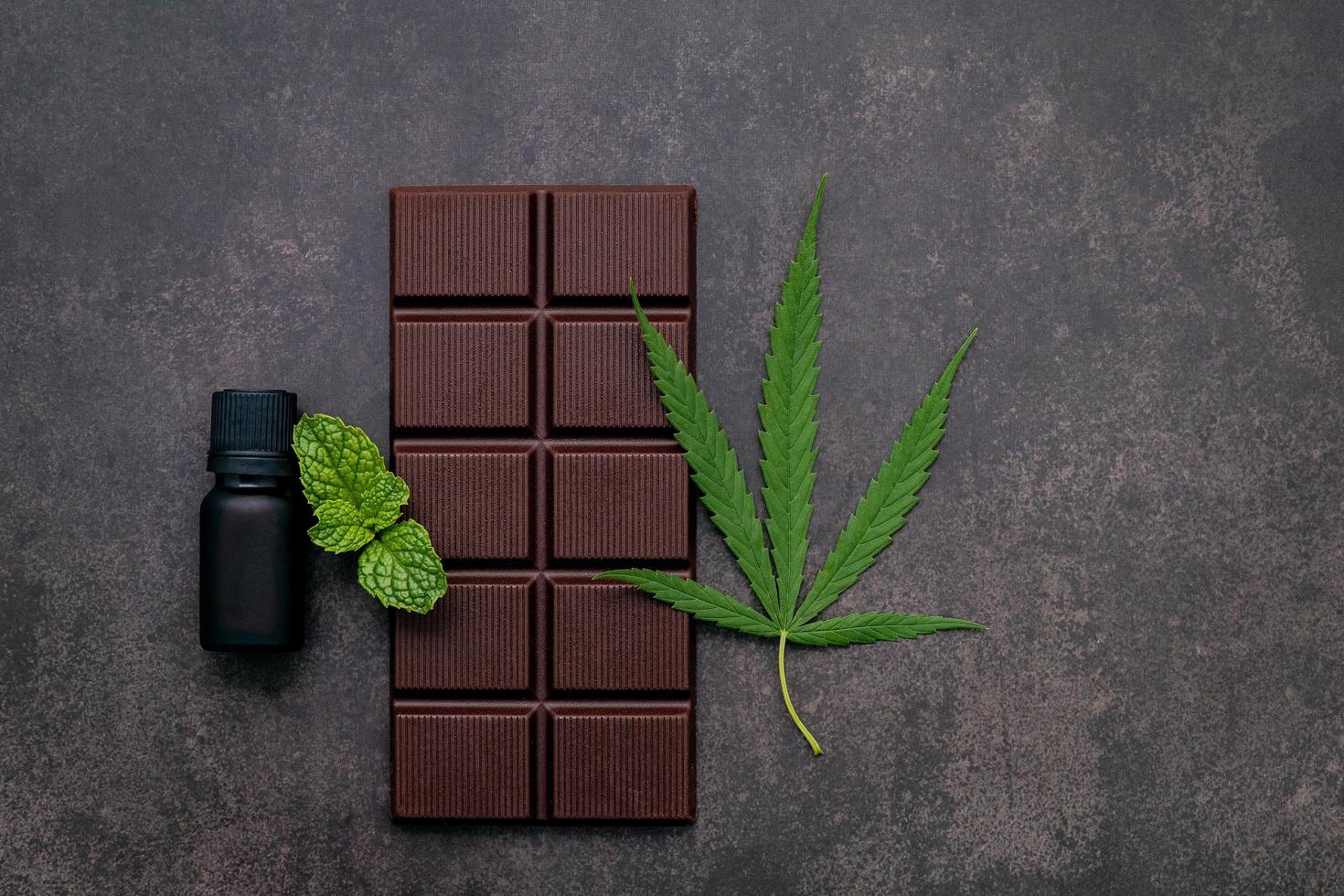 Hoja de cannabis con chocolate negro, hojas de plantas y utensilios de madera sobre un fondo de hormigón oscuro foto