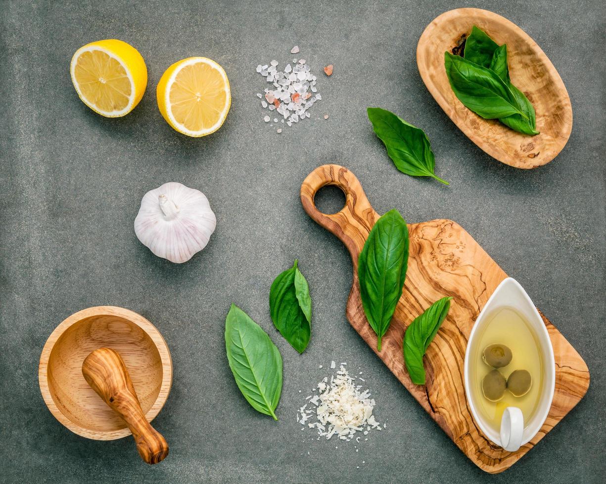 Ingredients for homemade pesto sauce of basil, parmesan cheese, garlic, olive oil, lemon, and Himalayan salt over a dark concrete background photo