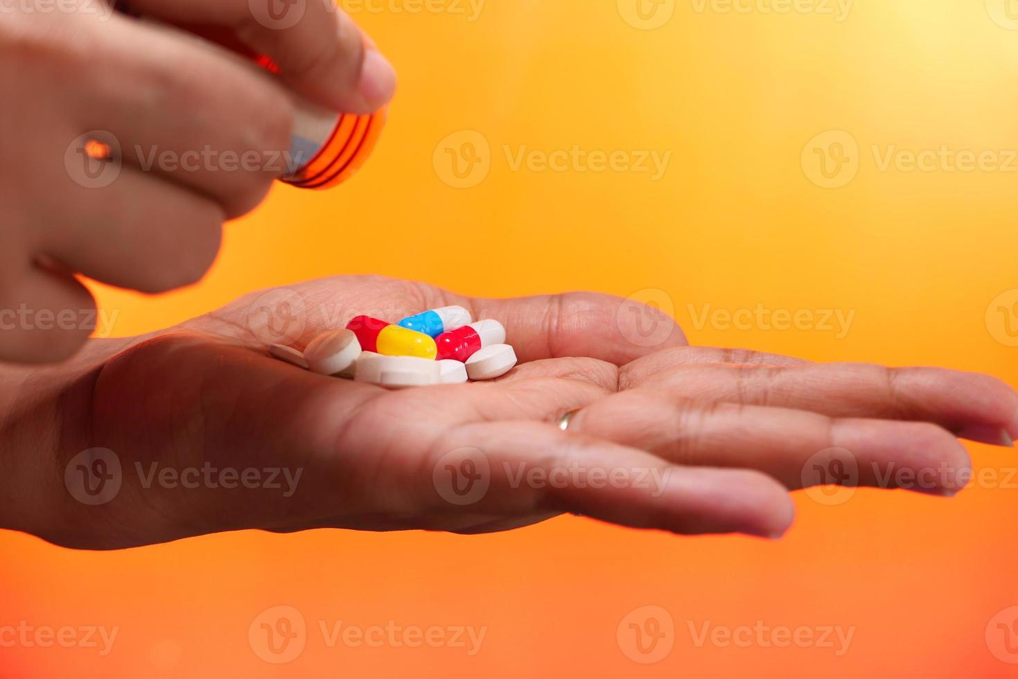 Cerca de las manos de la mujer tomando pastillas sobre fondo naranja foto