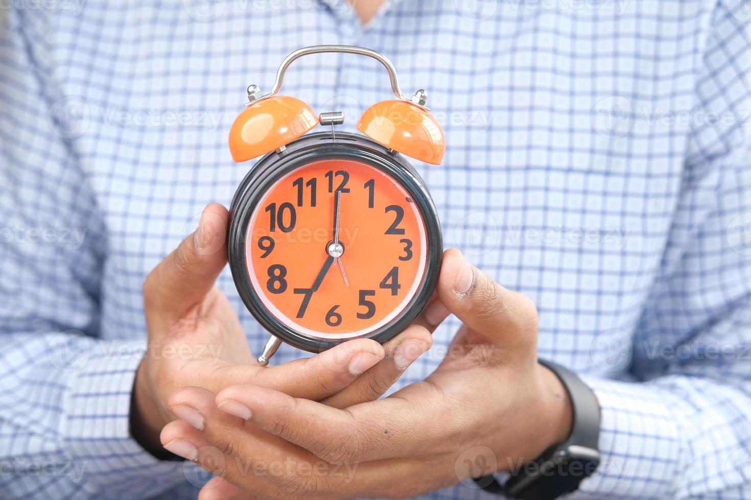 Man's hand holding orange alarm clock photo