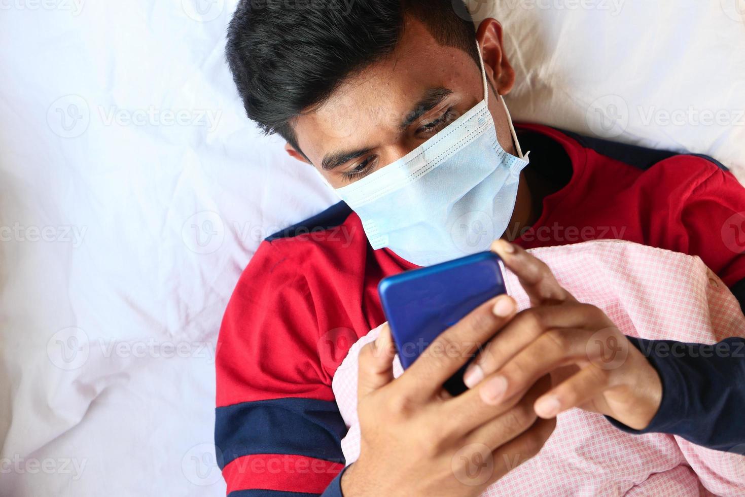 Hombre enfermo en mascarilla quirúrgica con teléfonos inteligentes. foto