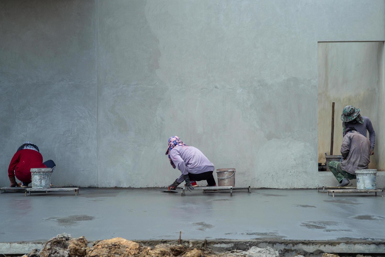 Retrato posterior de un grupo de trabajadores que utilizan paletas para pavimentar la superficie del cemento foto