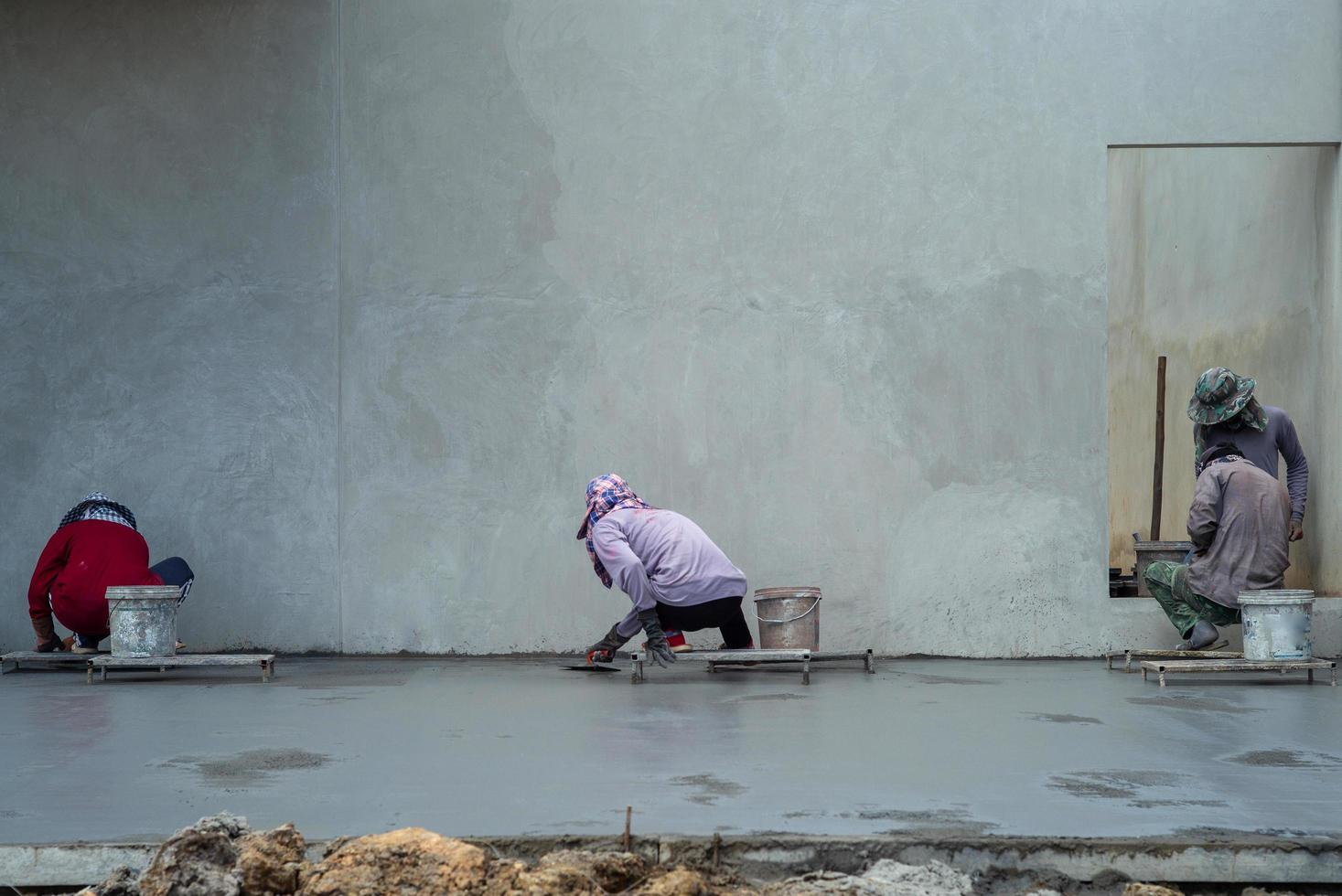 Back portrait of a group of workers using trowels for flooring the cement surface photo