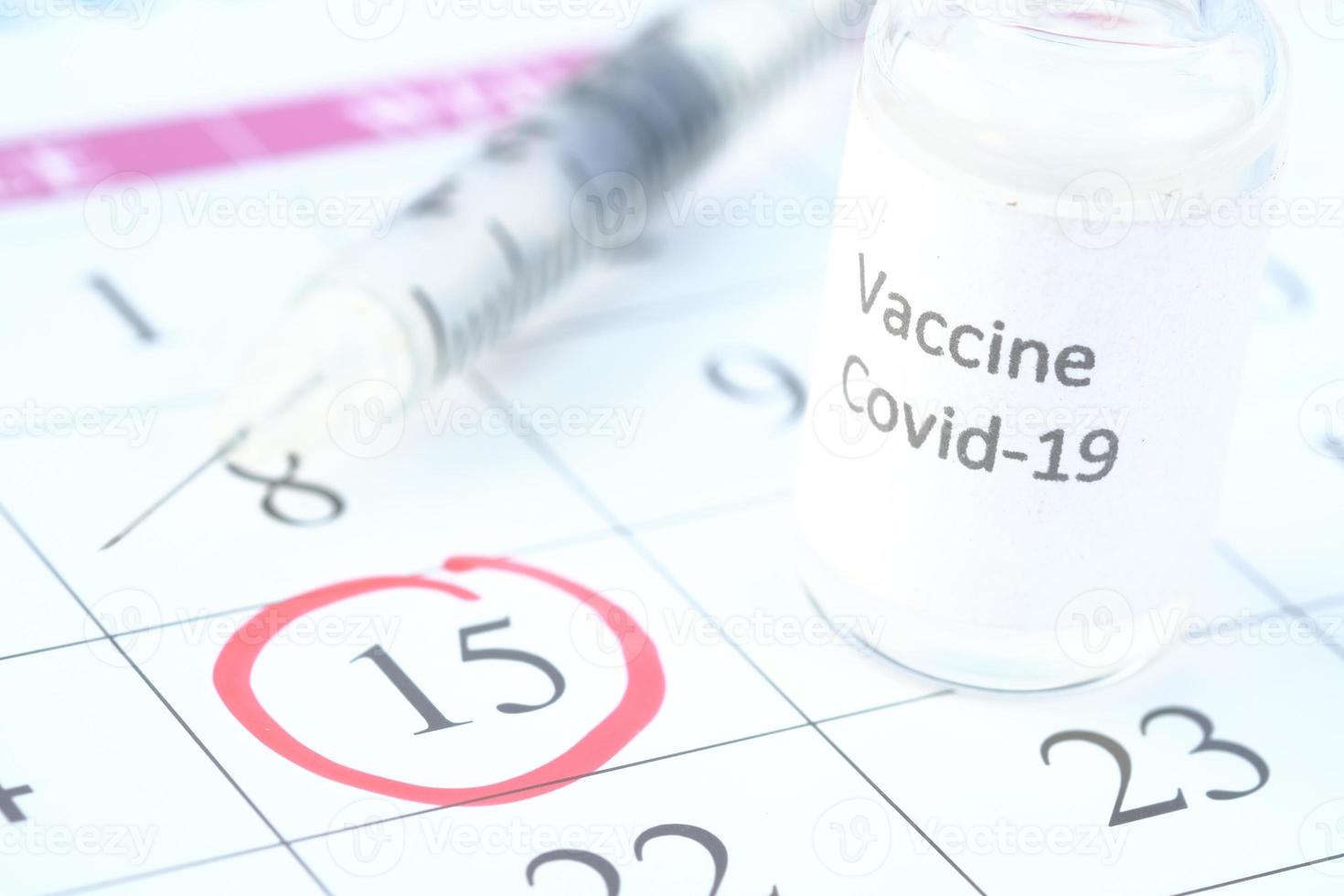 Close up of coronavirus vaccine and syringe on a calendar with red circle photo