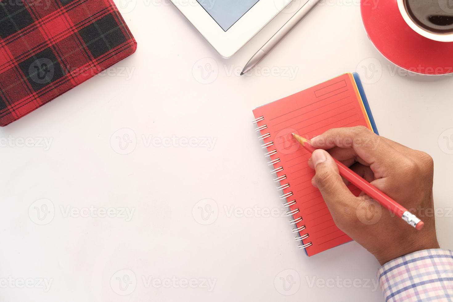 Man's hand writing on red notepad with pencil photo