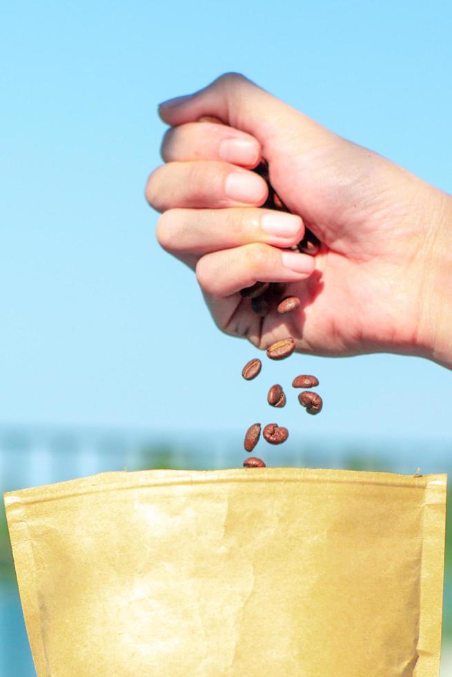 Primer plano de la mano liberando los granos de café en la bolsa de papel marrón foto