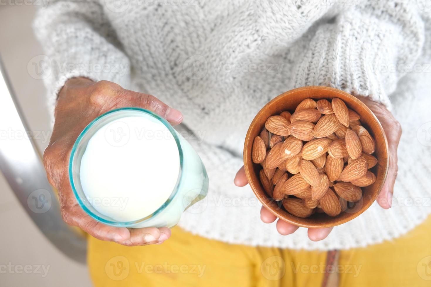 Senior woman's hand holding a bowl of almonds and glass of milk photo