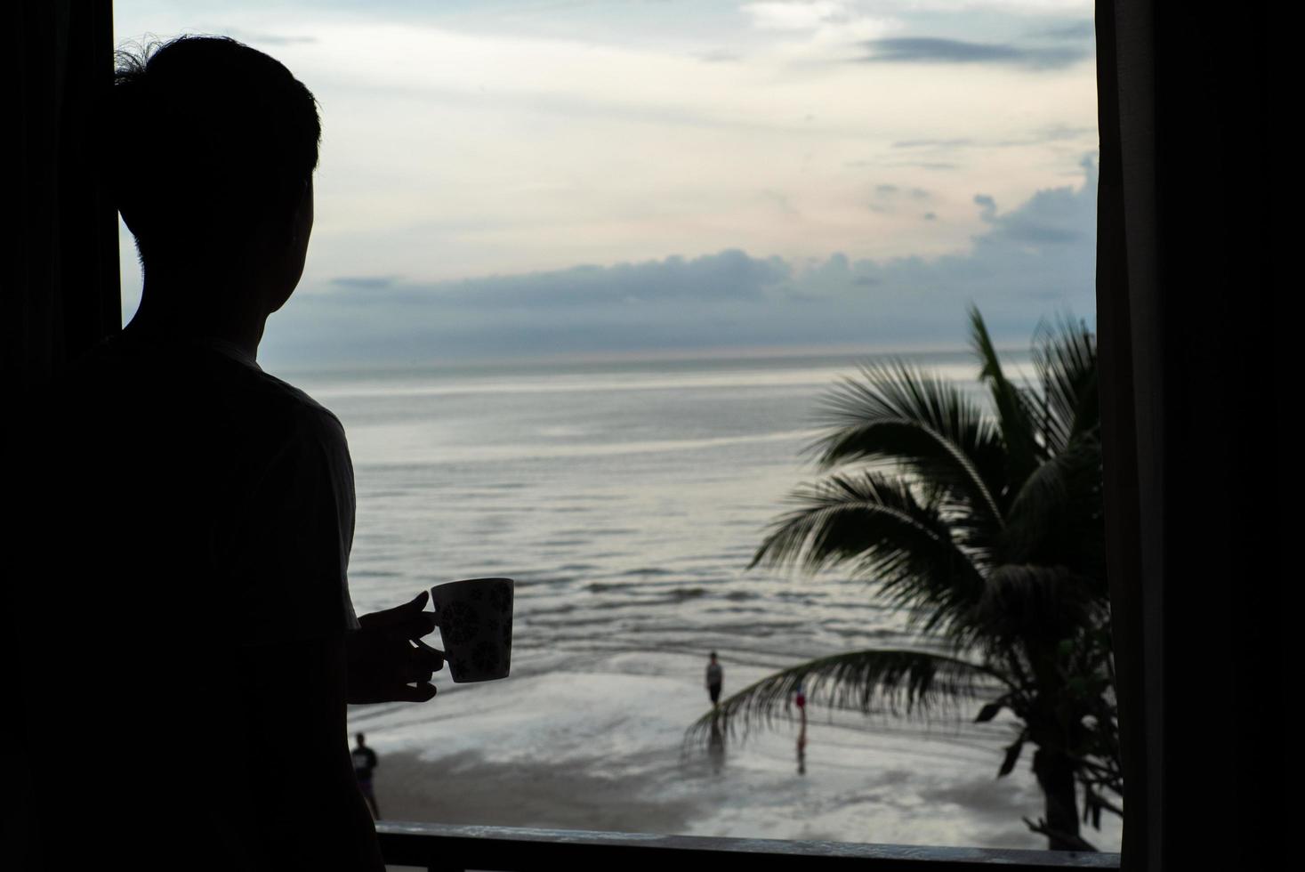 Silhouette of man holding the coffee cup and looking at the sea from the bedroom photo