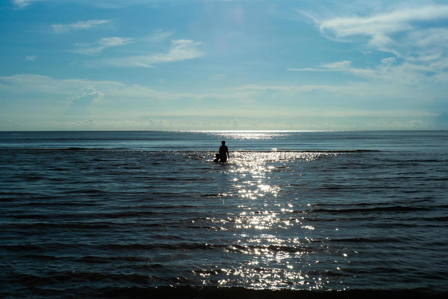 Imagen de silueta de gente caminando en el mar con reflejo de sol foto