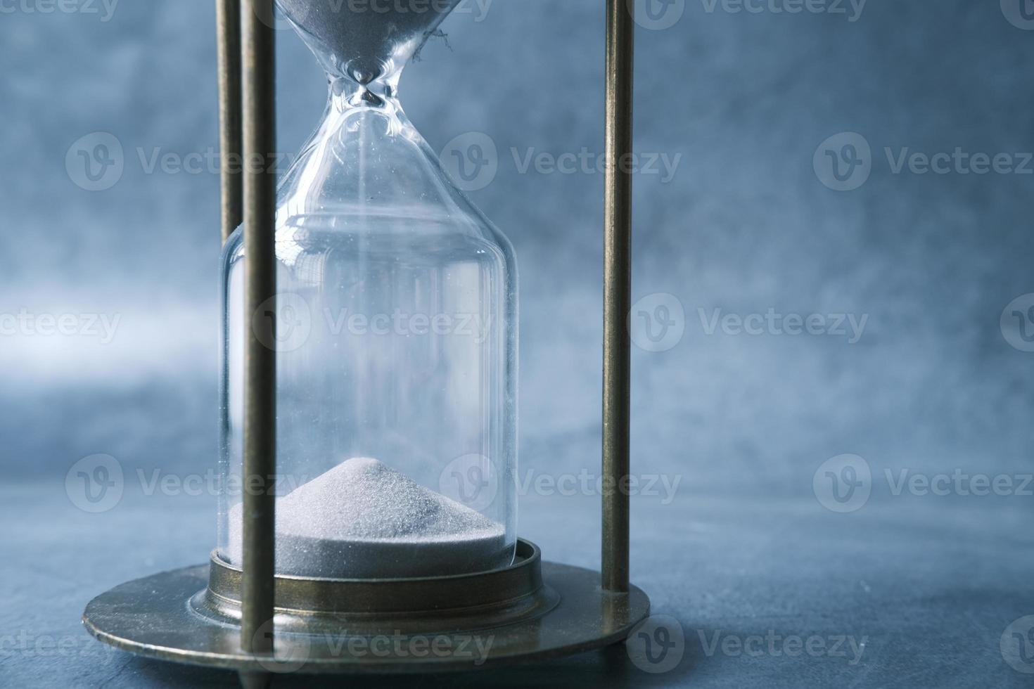 Sand flowing through hourglass on table photo