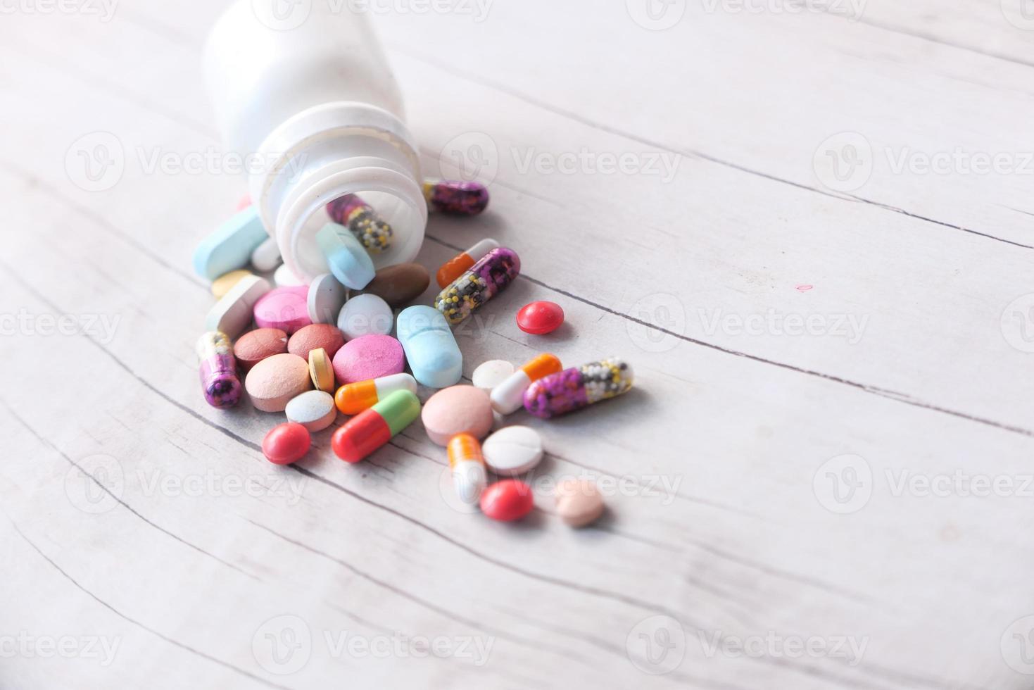 Colorful pills spilling on wooden background photo