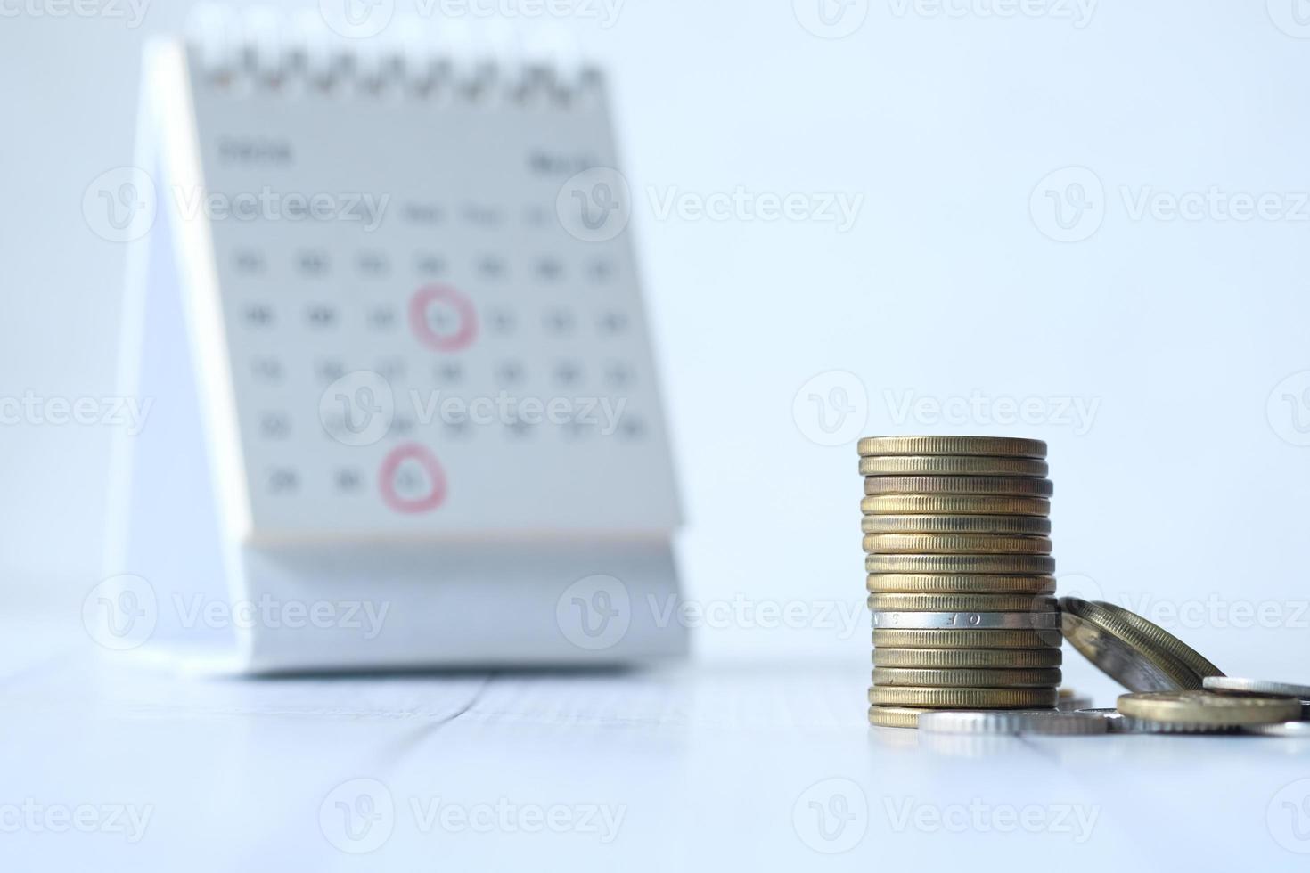 Concepto de fecha límite con pila de monedas y calendario sobre fondo blanco. foto