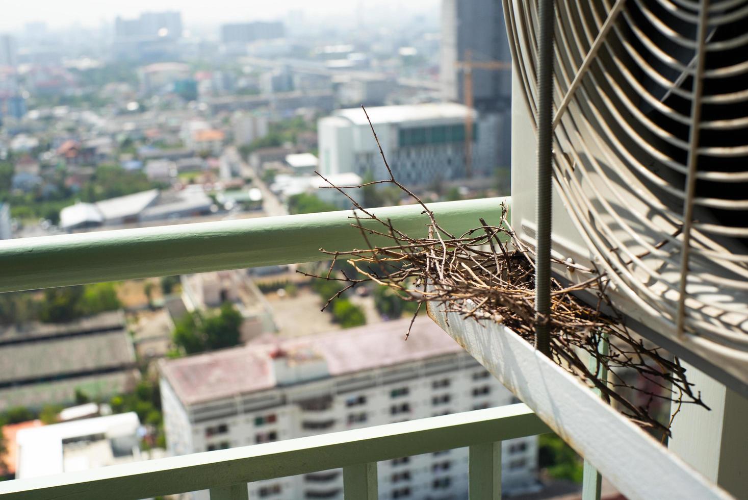 Closeup bird nest on the steel cage of air conditioner at the terrace of high condominium with blurred cityscape background photo