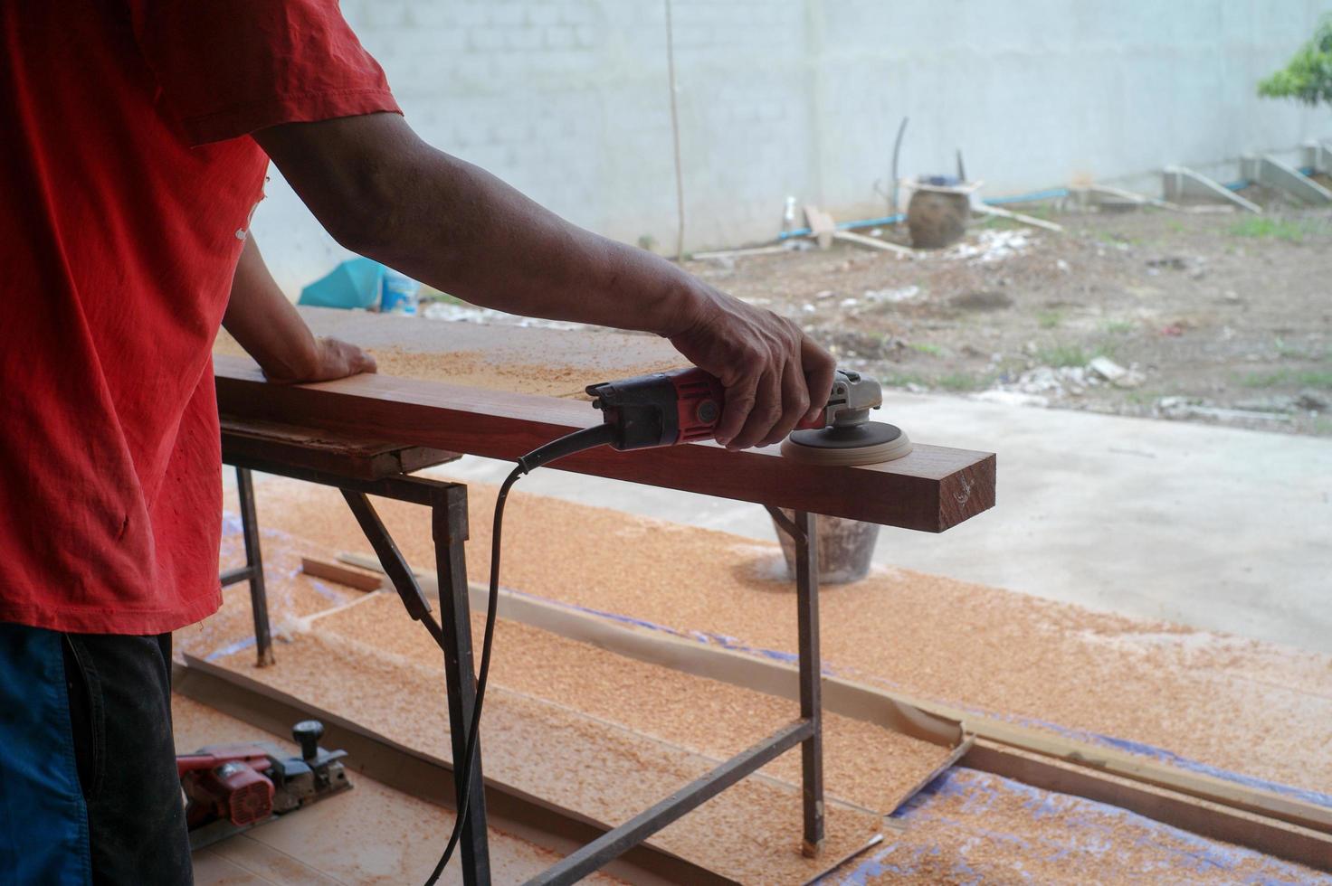 Primer plano de la mano del carpintero sostiene la herramienta eléctrica fregando la superficie de la madera foto