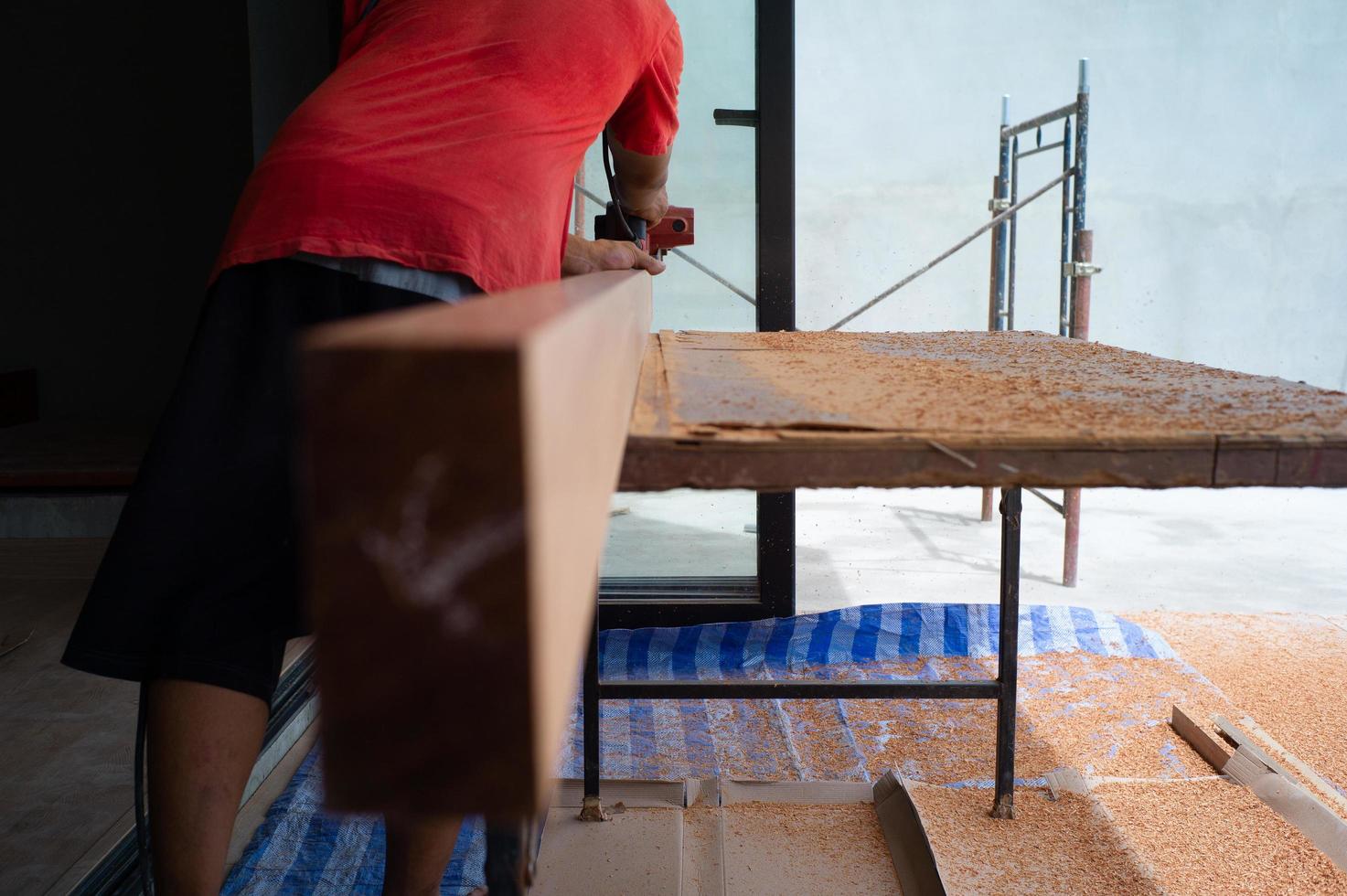 Back portrait of carpenter holds electrical tool scrubbing the surface of wood for woodwork at the construction site photo