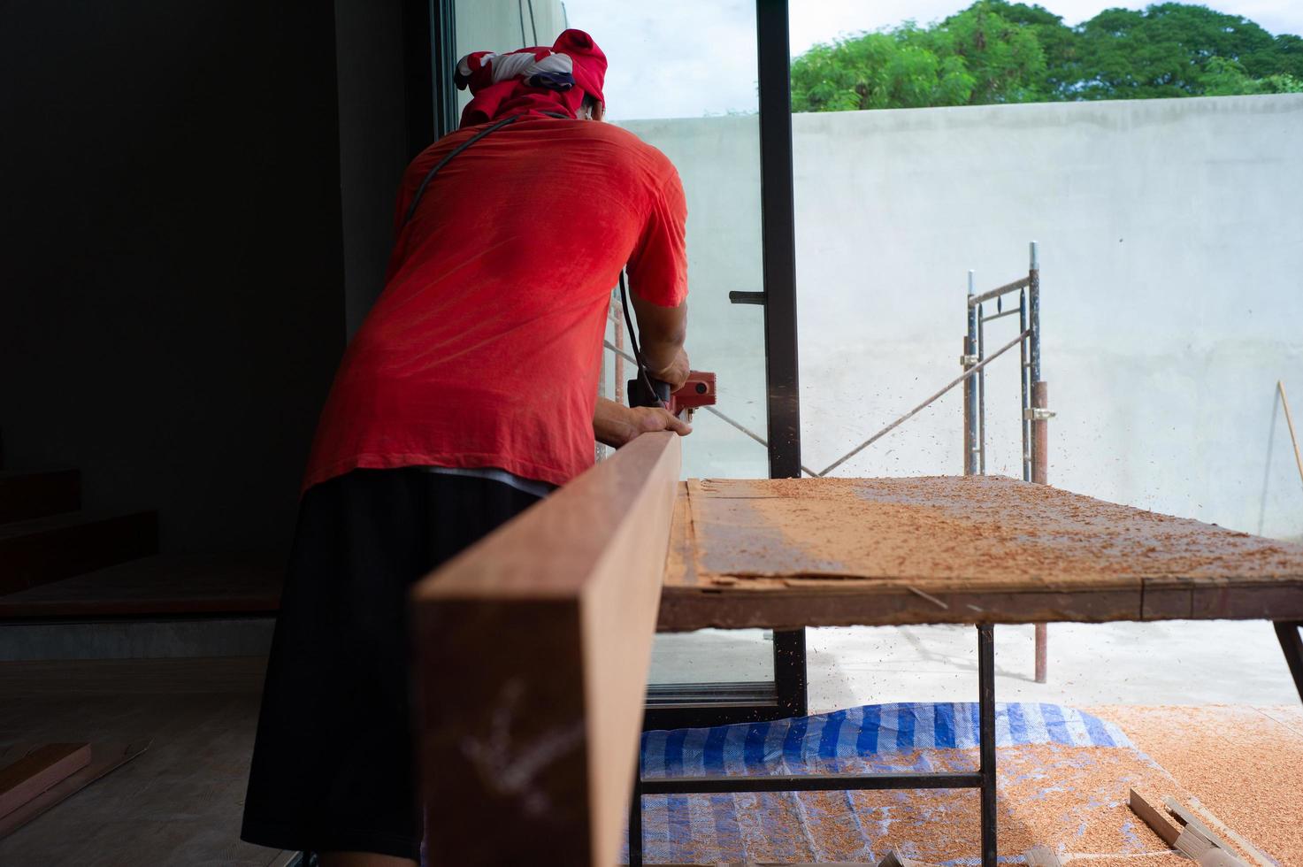 Back portrait of carpenter holds electrical tool scrubbing the surface of wood for woodwork at the construction site photo