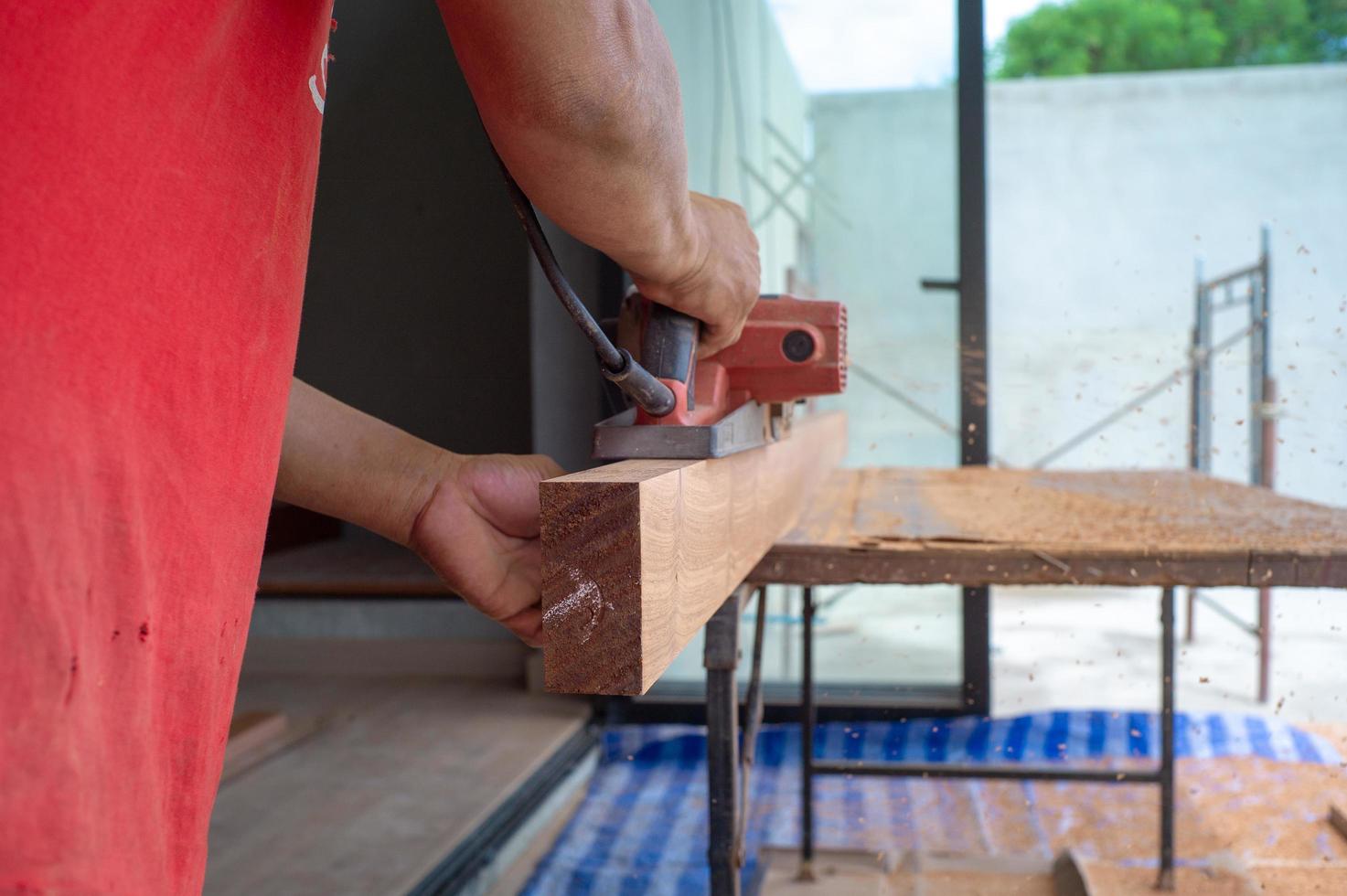 Closeup hand of carpenter holds electrical tool scrubbing the surface of wood photo