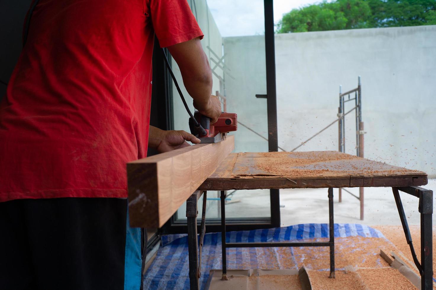 Primer plano de la mano del carpintero sostiene la herramienta eléctrica fregando la superficie de la madera foto