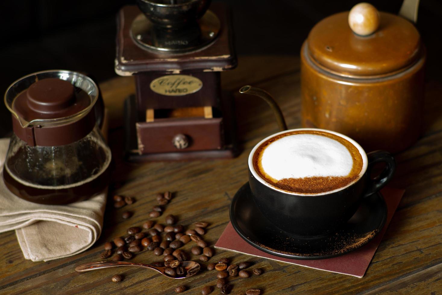 Closeup top view of hot cappucino cup with selective focus on coffee beans on wooden table with blurred grinder background photo