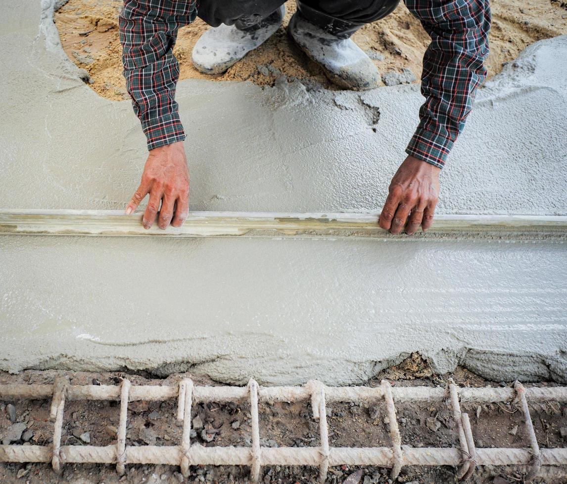 Trabajador con llana de madera para nivelar el piso de concreto foto