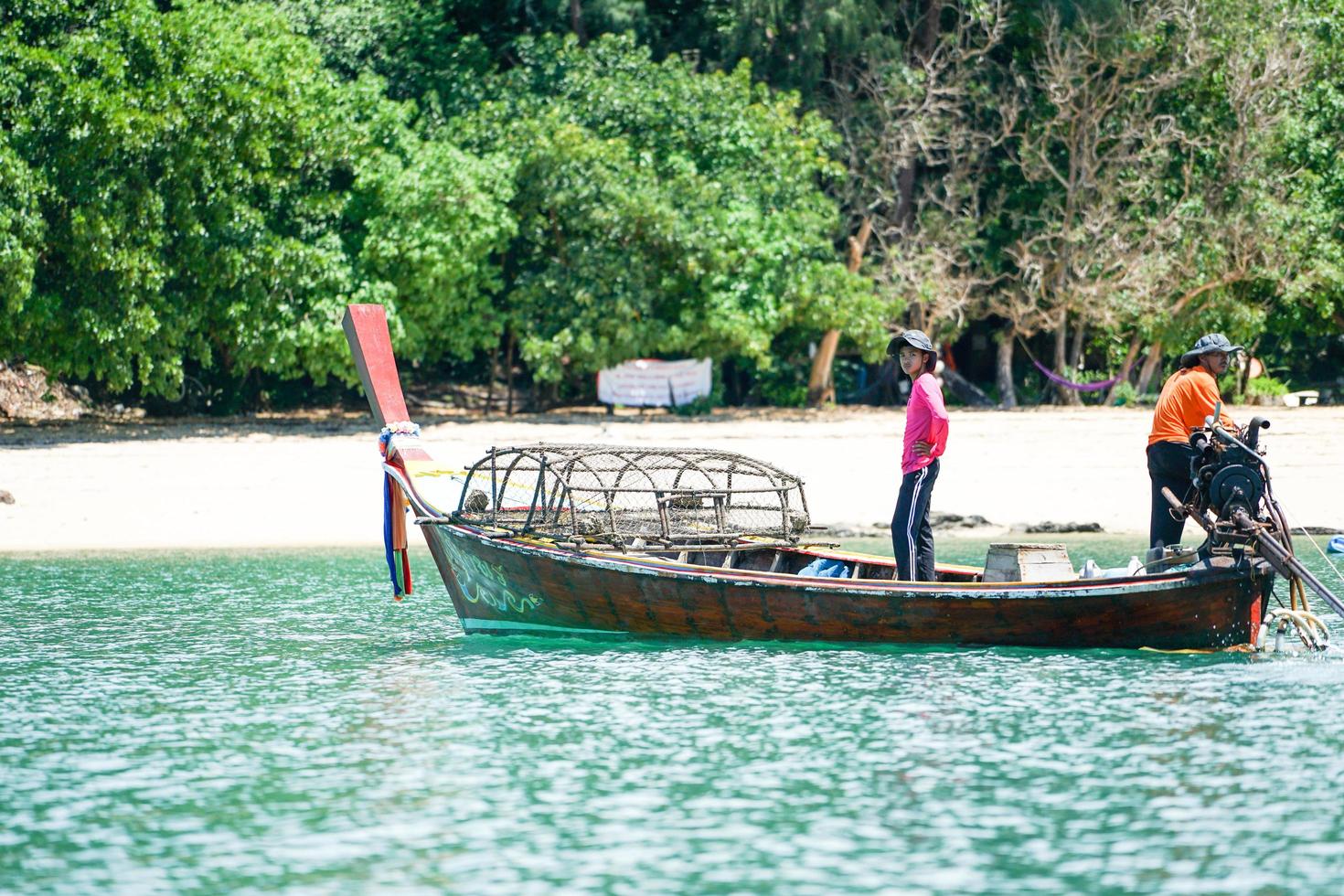 Ko Lanta, Krabi, Tailandia 2019: los pescadores conducen el tradicional bote de cola larga y encuentran peces con herramientas en un día soleado con una isla desenfocada de fondo foto