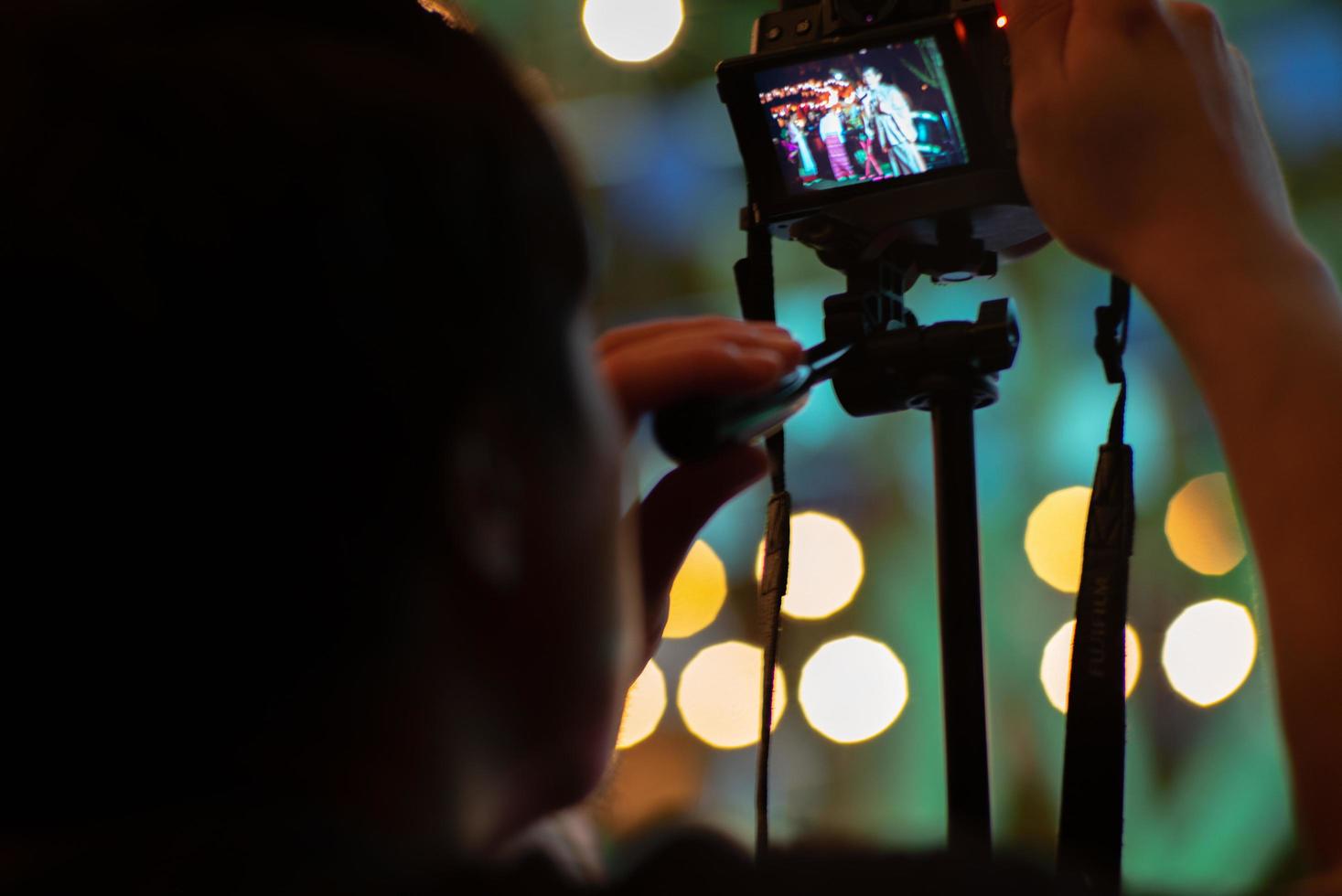 Manos de turista grabando el video por la cámara en el trípode con brillantes luces bokeh de fondo foto