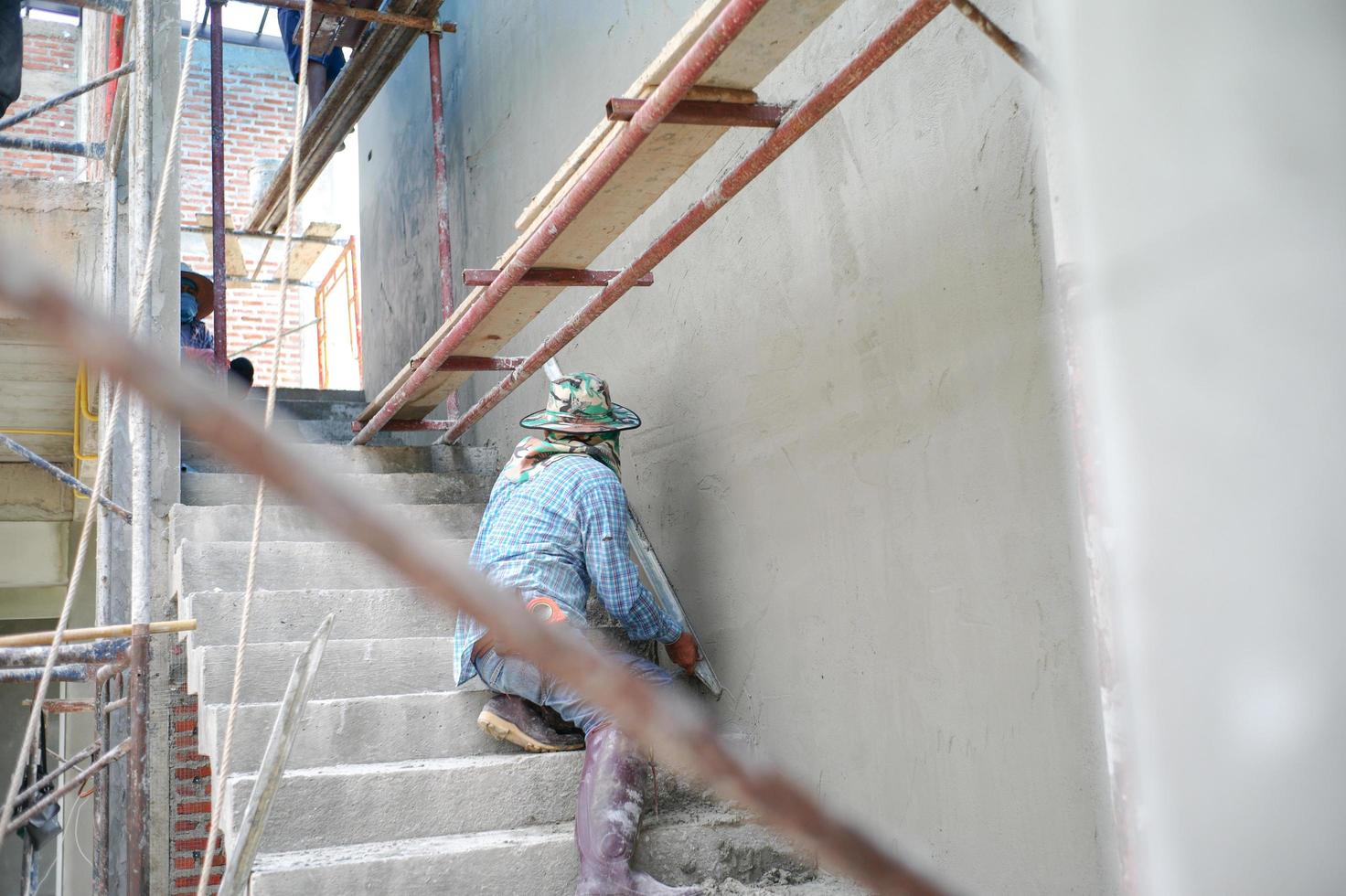 Group of workers stand on the steel scaffolding and builds plastered cement wall in the house under construction photo