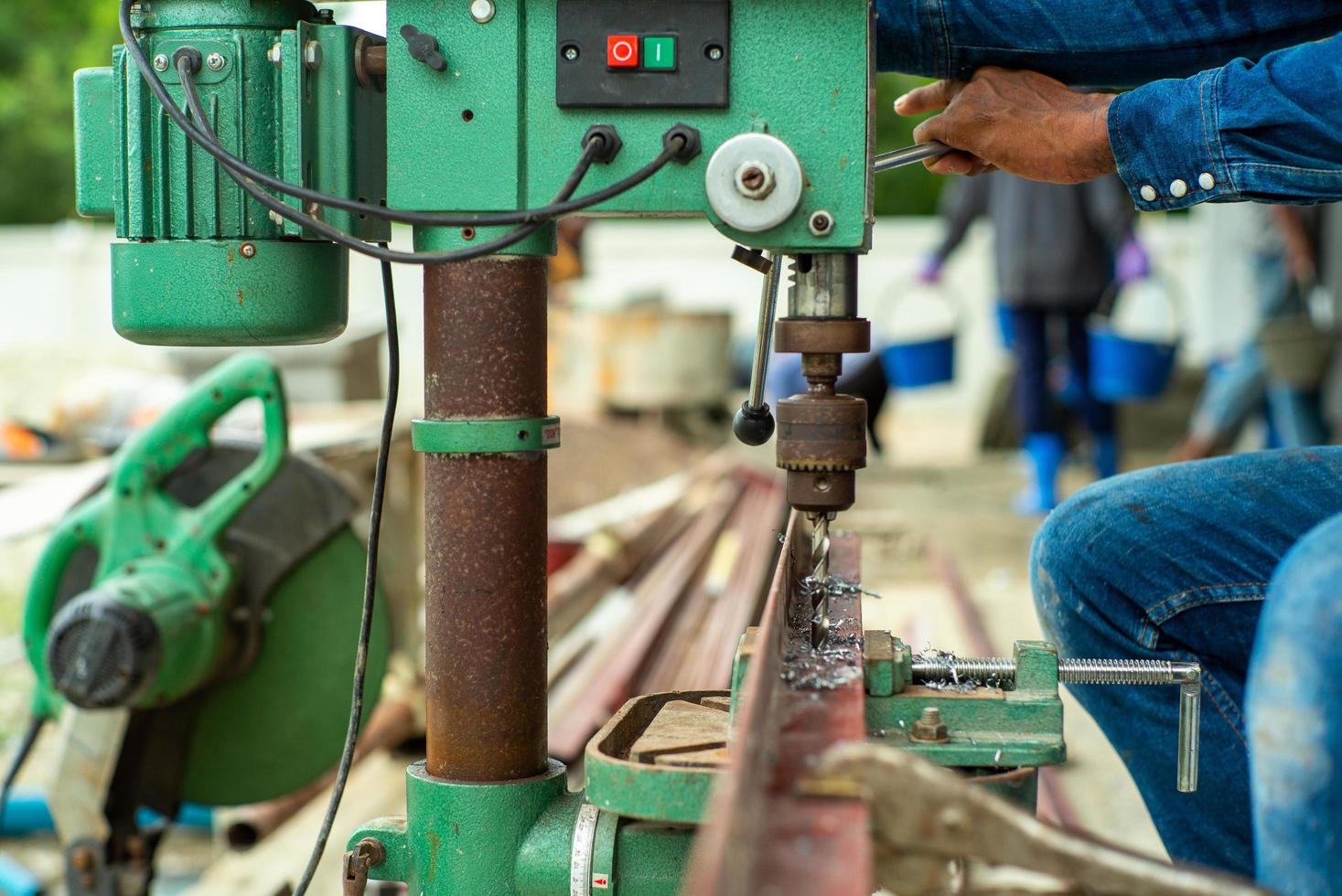 Closeup selective focus on hands of worker controls the electrical drilling machine for drilling the hole on the angle steel bar at the construction site photo