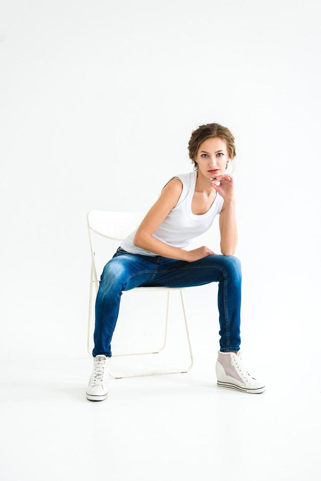Cheerful girl in a white t-shirt and dark blue jeans in the studio on a white background photo