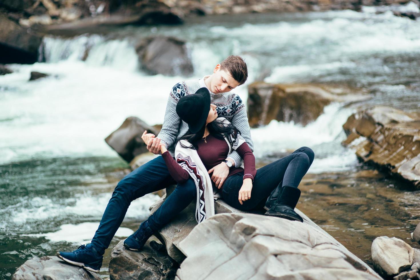 chico y chica en suéteres calientes caminando a lo largo de un río de montaña, historia de amor foto