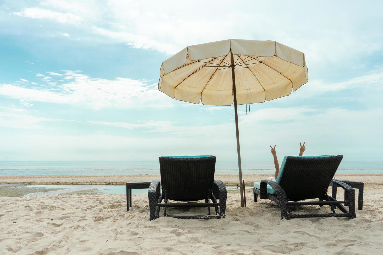 Back portrait of little girl lying on a beach bench and showing her fingers in victory sign photo