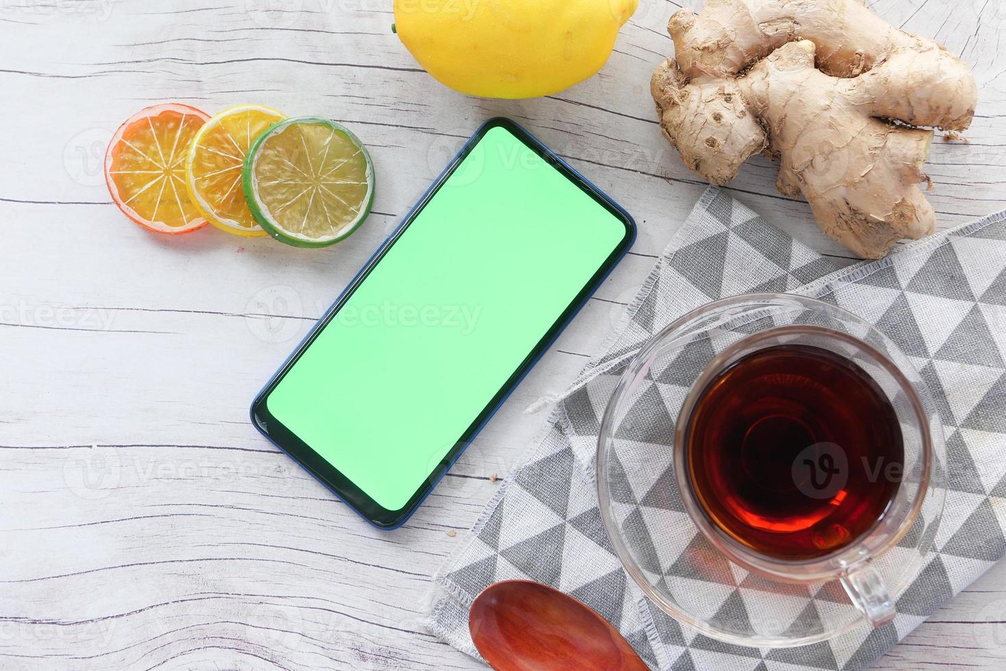 Vista superior del té de jengibre y teléfonos inteligentes con pantalla verde sobre fondo de madera foto